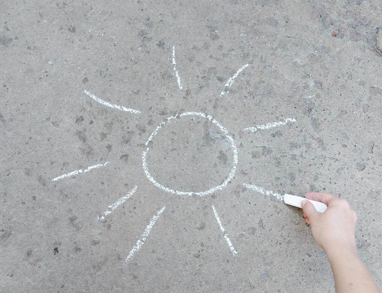 Hand zeichnet die Sonne mit Kreide auf den Bürgersteig. Kreativität, Sommer, Kreativität. foto