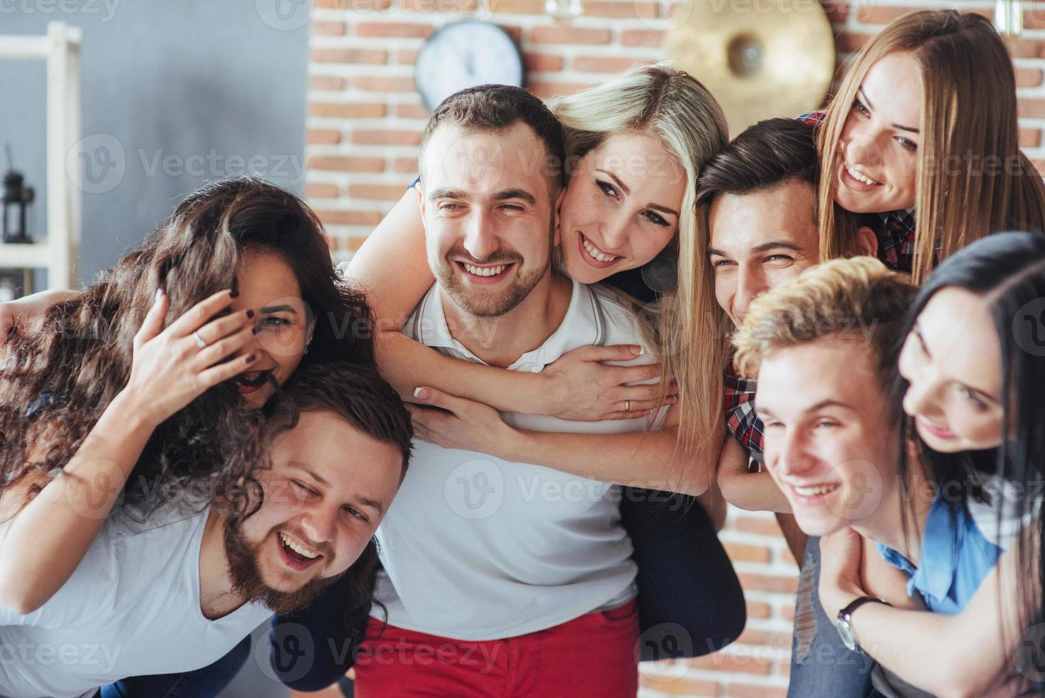 Gruppenporträt von multiethnischen Jungen und Mädchen mit farbenfrohen, modischen Kleidern, die einen Freund halten, der auf einer Ziegelwand posiert, Menschen im urbanen Stil, die Spaß haben, Konzepte über den Lebensstil der Jugendzusammengehörigkeit foto