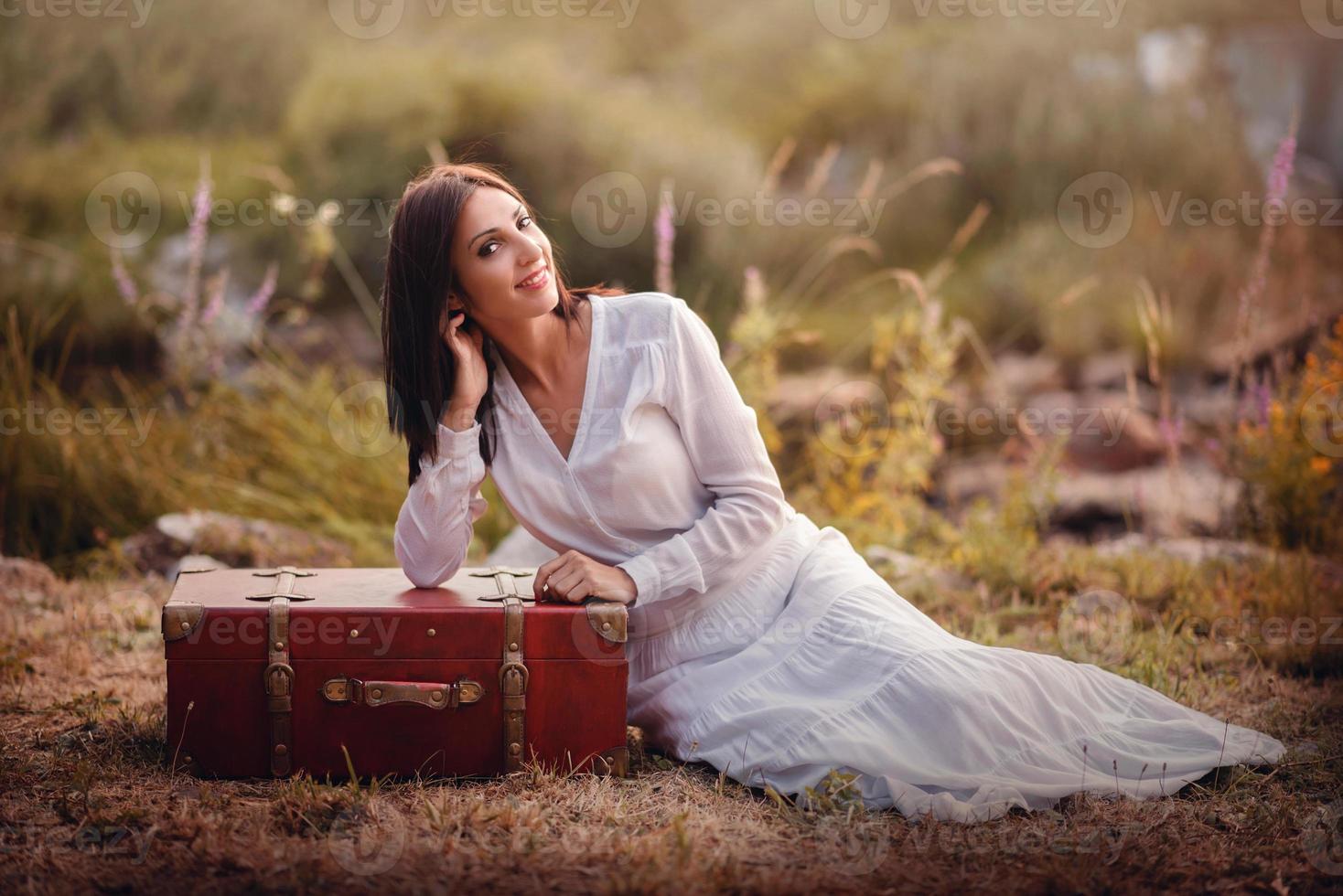 junge Frau, die mit Koffer auf dem Feld sitzt foto