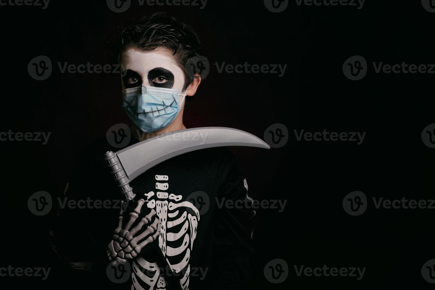 fröhliches halloween, kind mit medizinischer maske in einem skelettkostüm mit einer sense foto