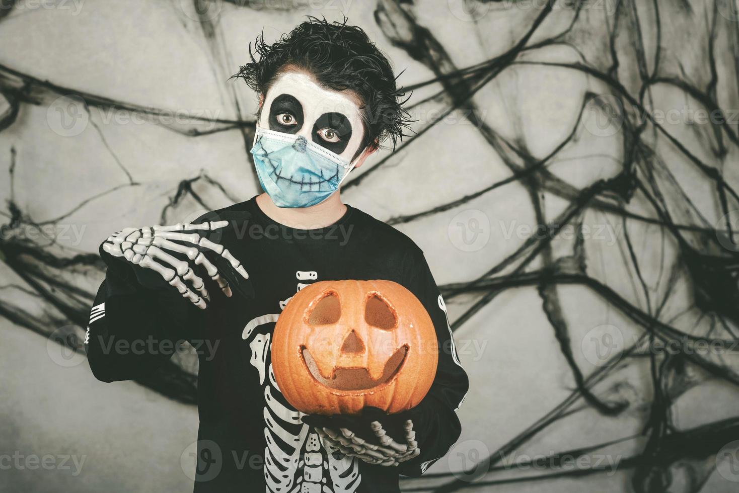 happy halloween.kid mit medizinischer maske in einem skelettkostüm mit halloween-kürbis foto