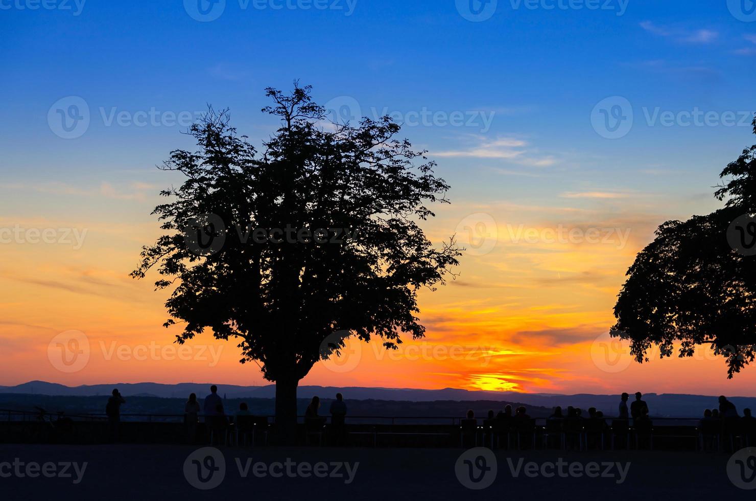 Silhouetten von Bäumen und Menschen, die einen erstaunlich bunten roten Sonnenuntergang beobachten foto