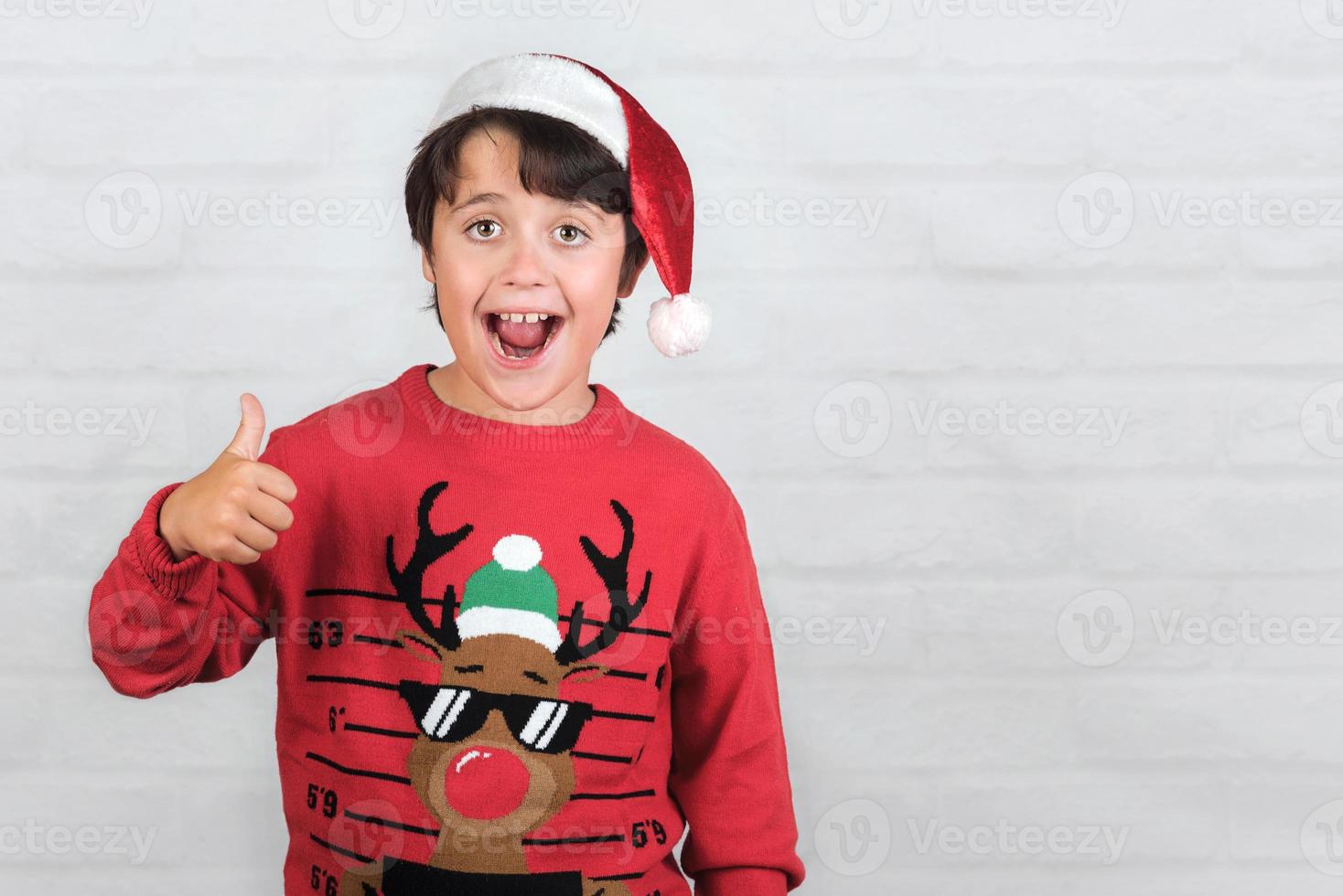 lächelndes Kind mit Weihnachtsmann-Hut, das den Daumen nach oben zeigt foto