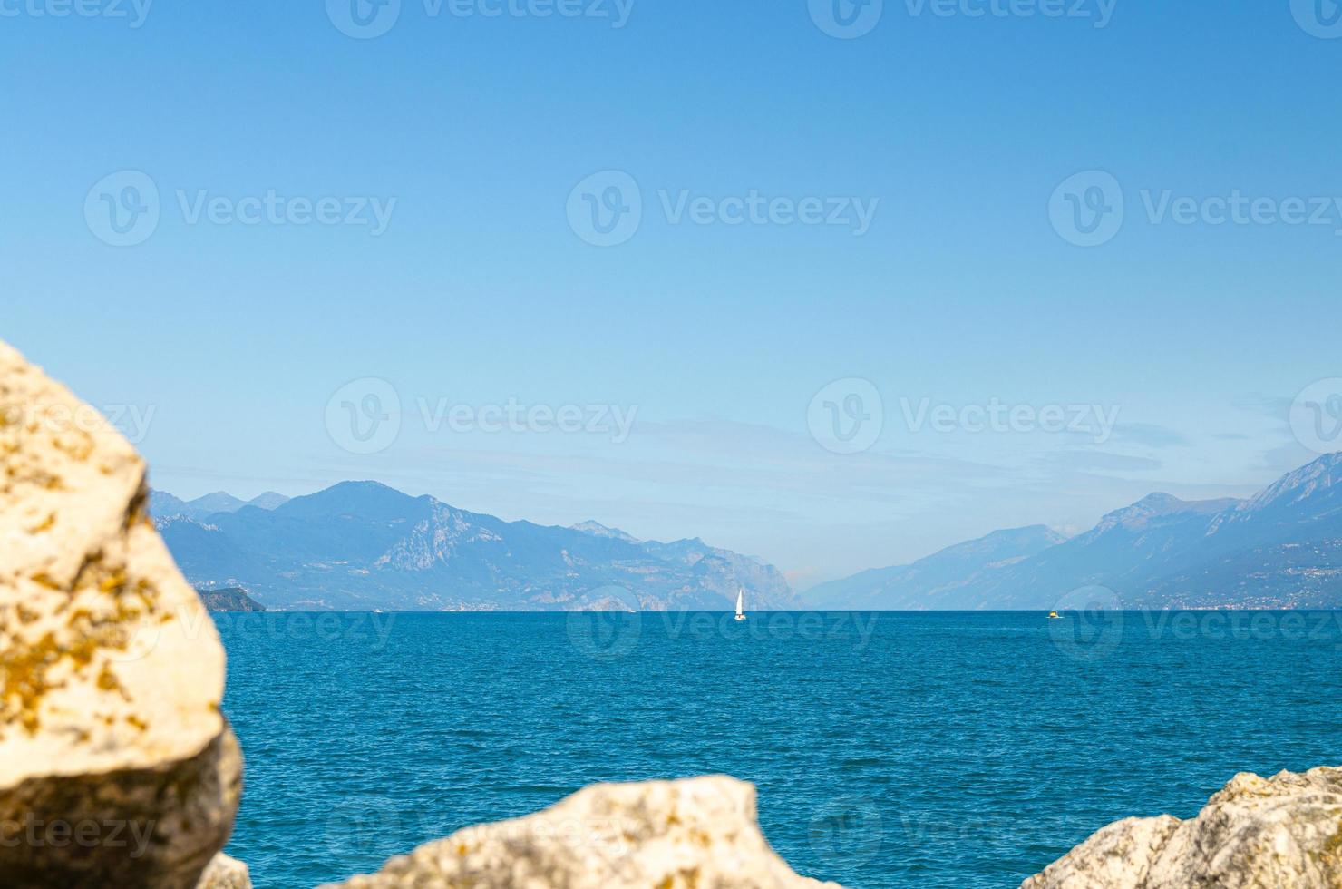 Kleine Segelyacht auf dem azurblauen Wasser des Gardasees mit dem Monte Baldo-Gebirge foto