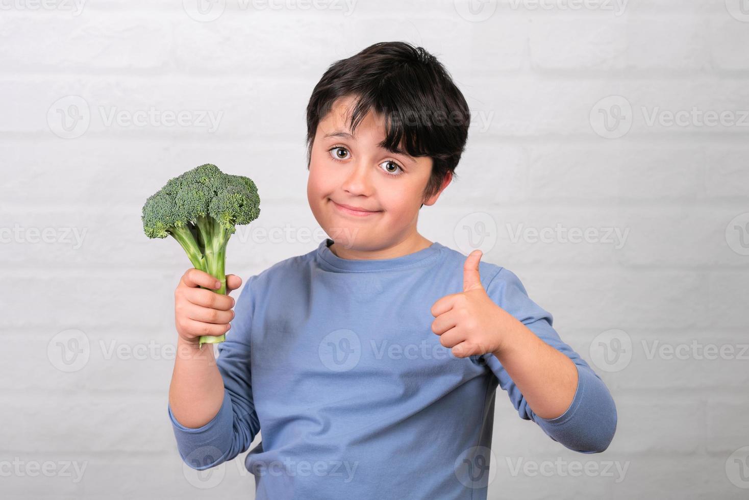 glückliches kind mit brokkoli in der hand, die daumen nach oben zeigt. gesundes lebensmittelkonzept foto