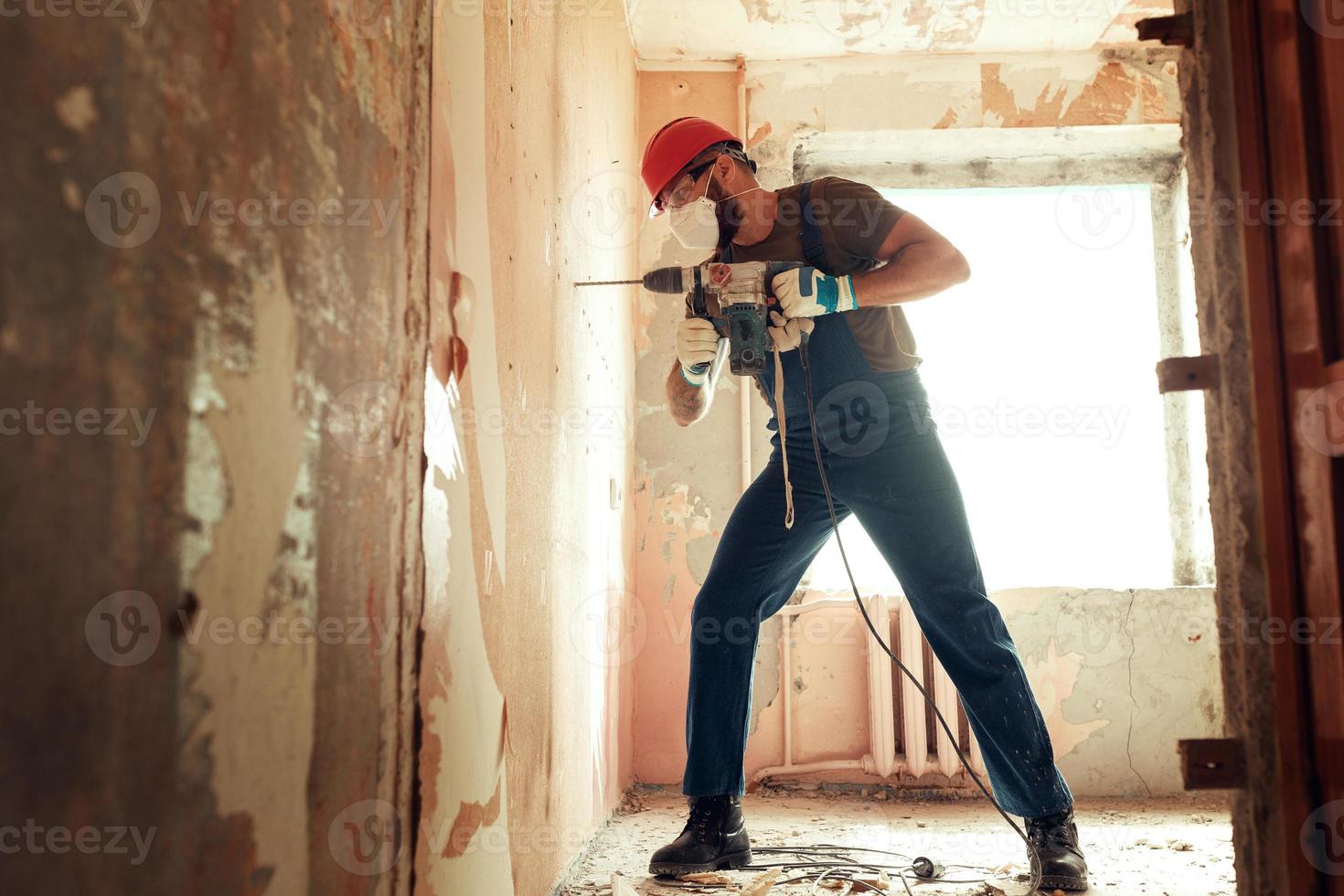 Baumeister mit Perforator bohrt Löcher in Betonwand foto