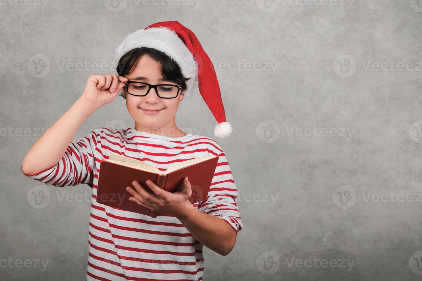 Frohe Weihnachten, lächelndes Kind mit Weihnachtsmann-Hut, das ein Buch liest foto