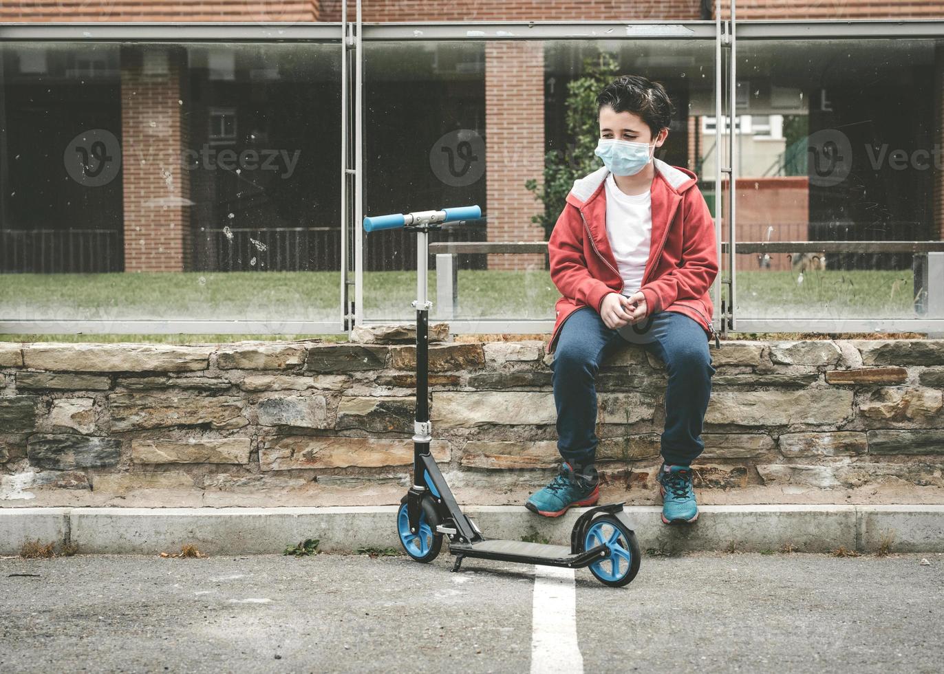 Kind mit medizinischer Maske mit seinem Roller in der Stadt foto