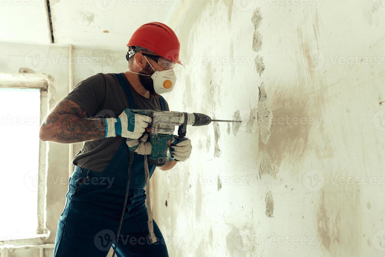 Baumeister mit Perforator bohrt Löcher in Betonwand foto