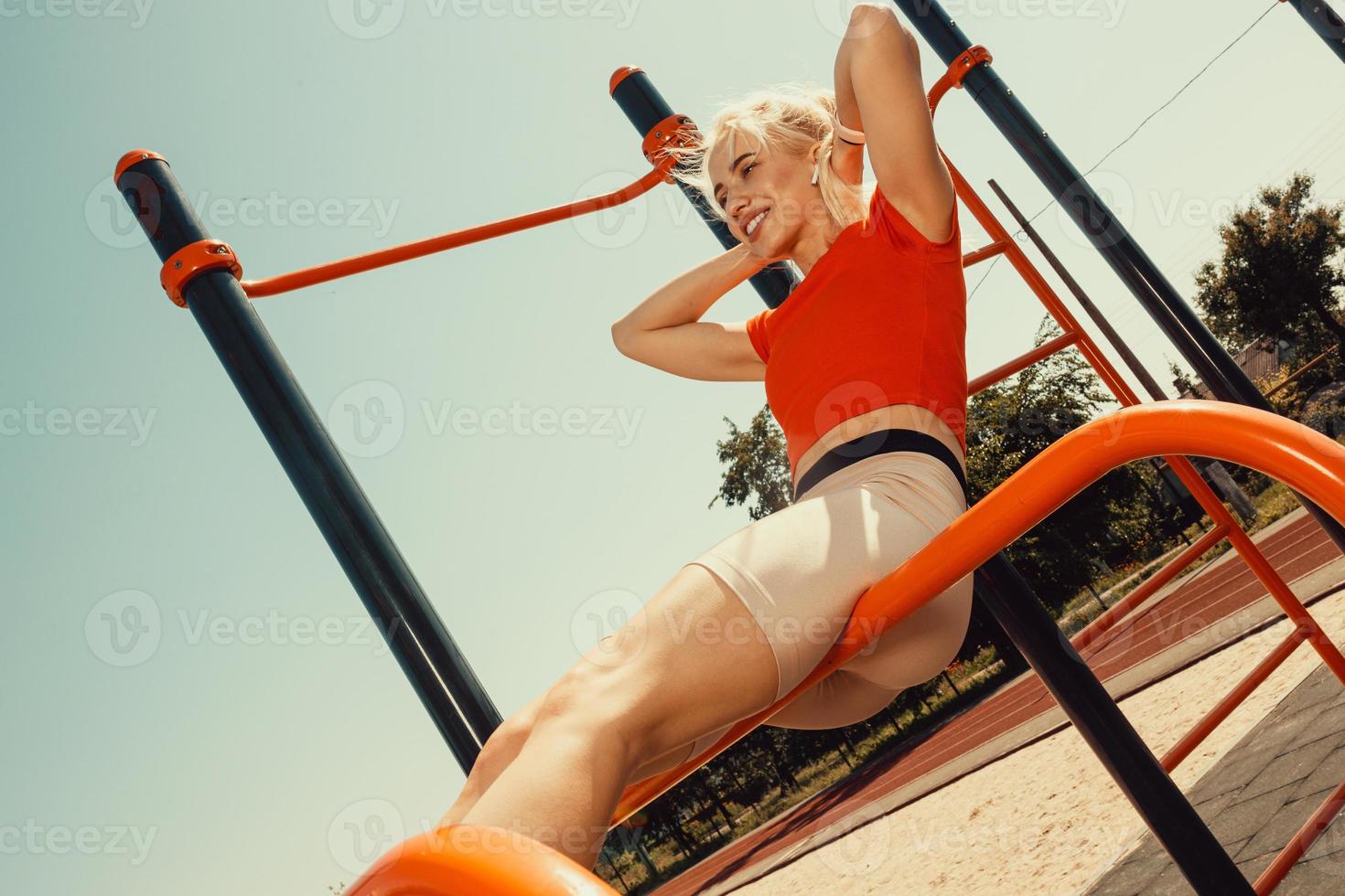 Schöne Blondine schüttelt die Muskeln der Presse an den horizontalen Balken foto