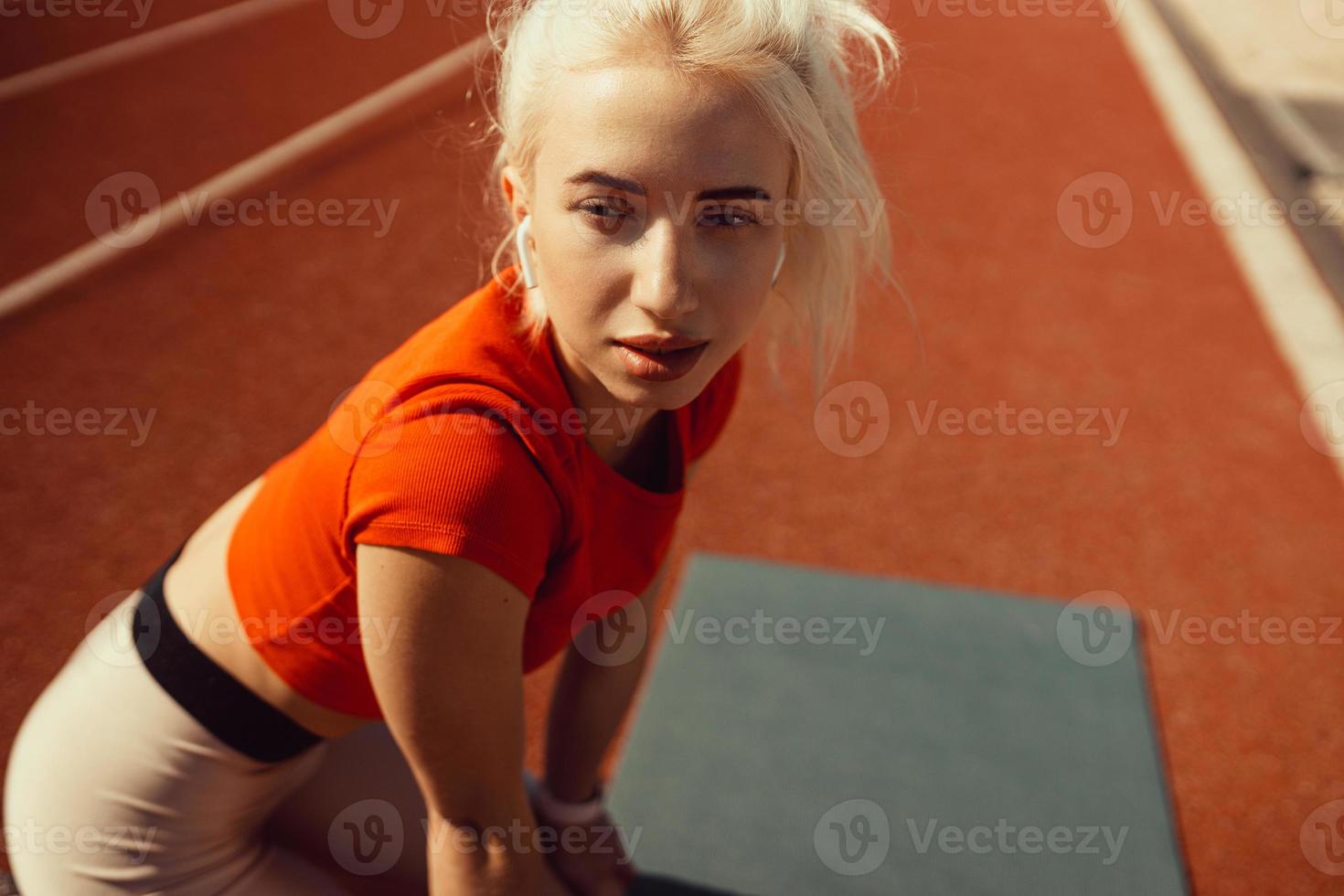 Nahaufnahmeporträt einer schönen Blondine, die auf einer Joggingstrecke sitzt foto