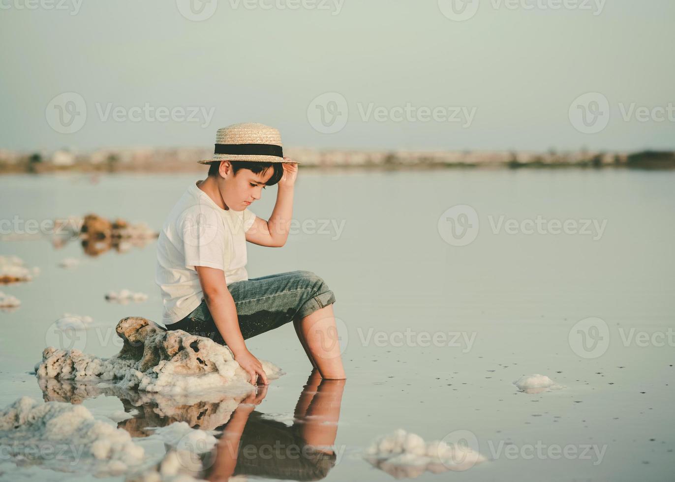 Trauriger und nachdenklicher Junge, der am Strand sitzt foto