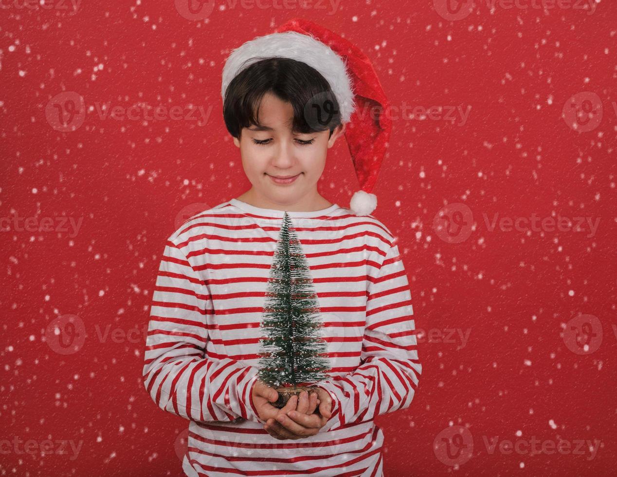 frohe weihnachten, kind mit weihnachtsmannmütze mit einem kleinen weihnachtsbaum in den händen foto