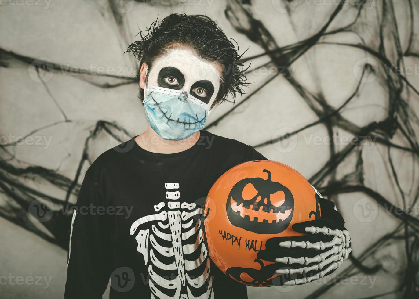 Fröhliches Halloween. Kind mit medizinischer Maske in einem Skelettkostüm mit Halloween-Ballon foto