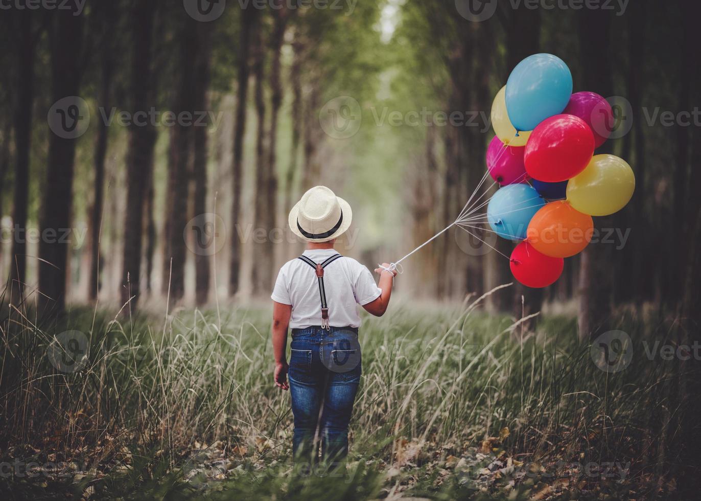 Rückansicht des nachdenklichen Kindes mit Luftballons im Wald foto
