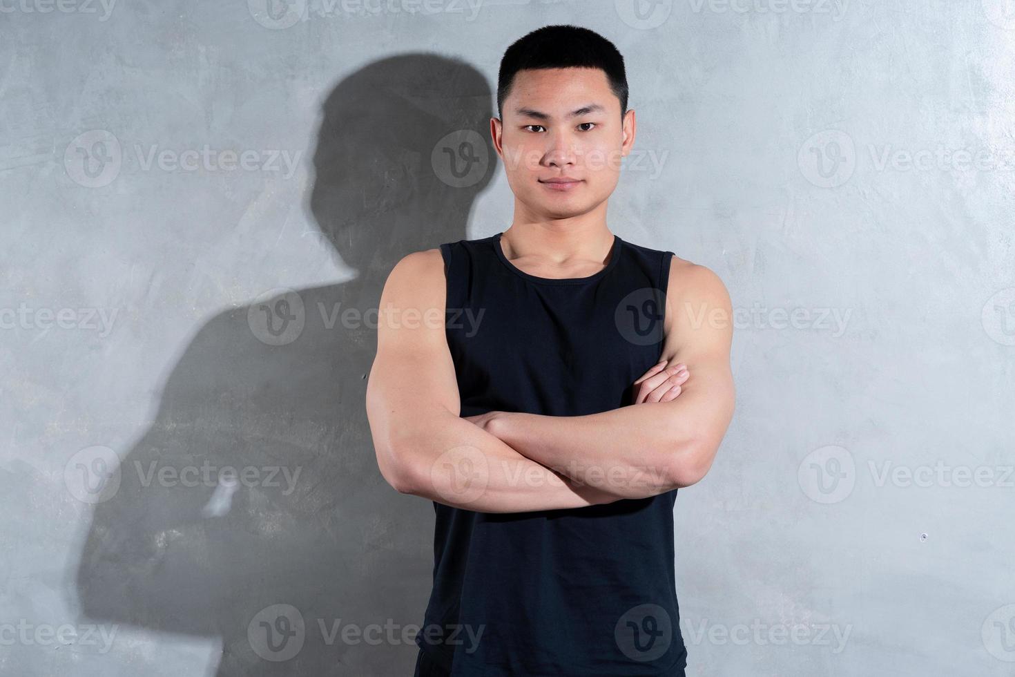 junger asiatischer persönlicher trainer, der auf grauem hintergrund aufwirft foto