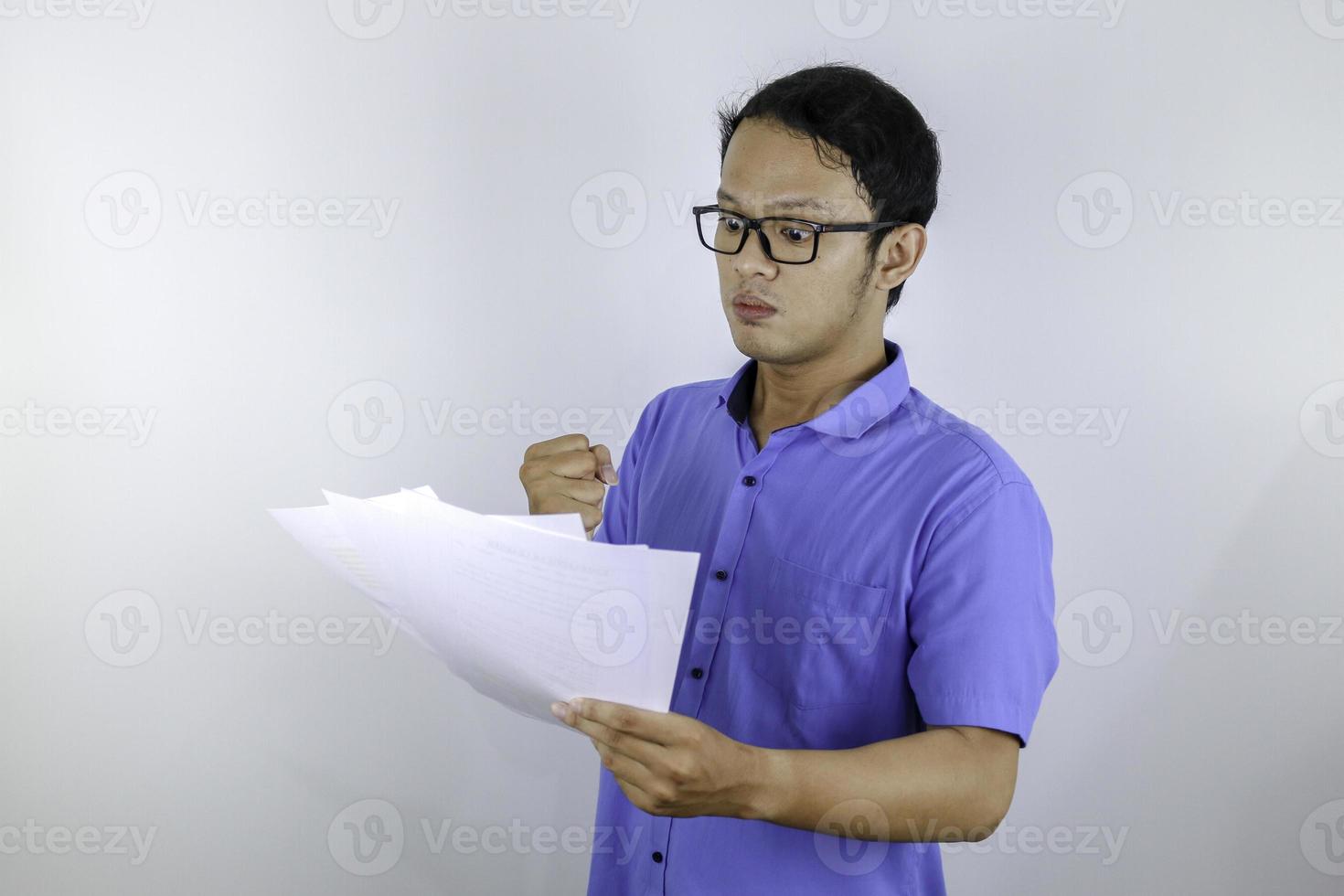 junger asiatischer mann ist wütend und wütend, wenn er auf papierdokument schaut. indonesischer Mann mit blauem Hemd. foto