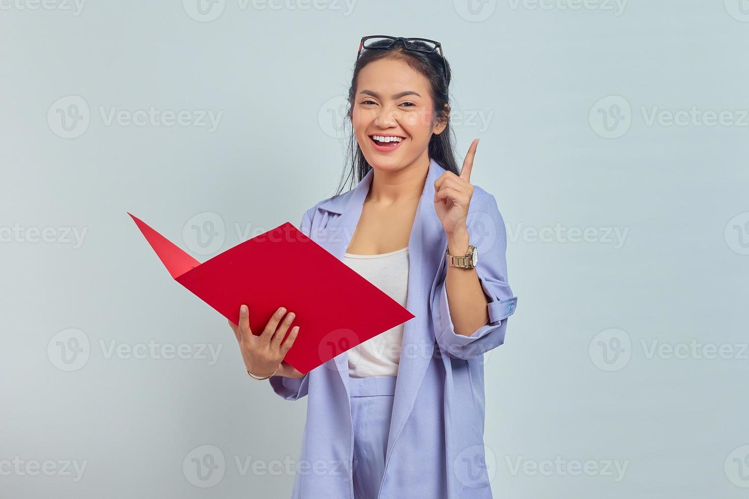 Porträt einer fröhlichen jungen asiatischen Geschäftsfrau, die einen Dokumentenordner hält und eine brillante Idee im Kopf hat, die auf violettem Hintergrund isoliert ist foto