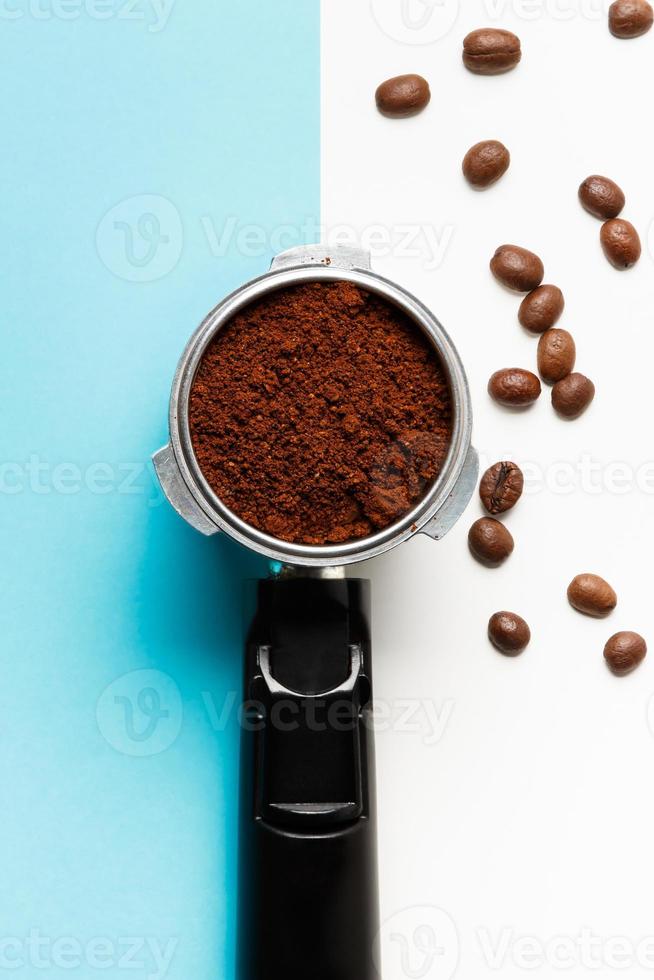 Filterhalter für Espressomaschine mit gemahlenem Kaffee und Kaffeebohnen auf blauem und weißem Hintergrund. foto