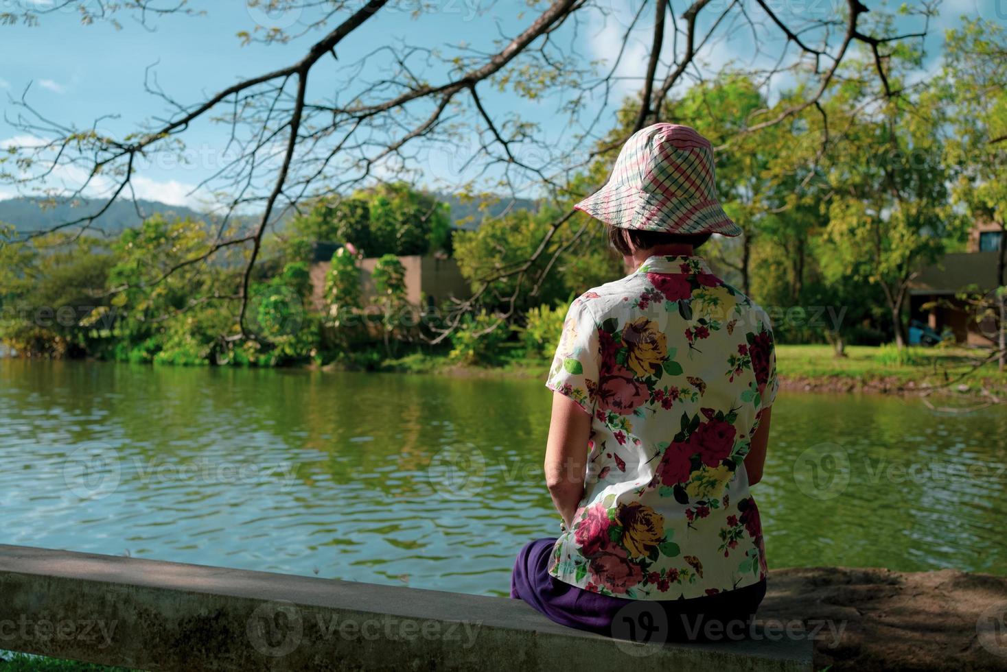 Rückansicht einer Seniorin, die am See sitzt und die Natur genießt foto