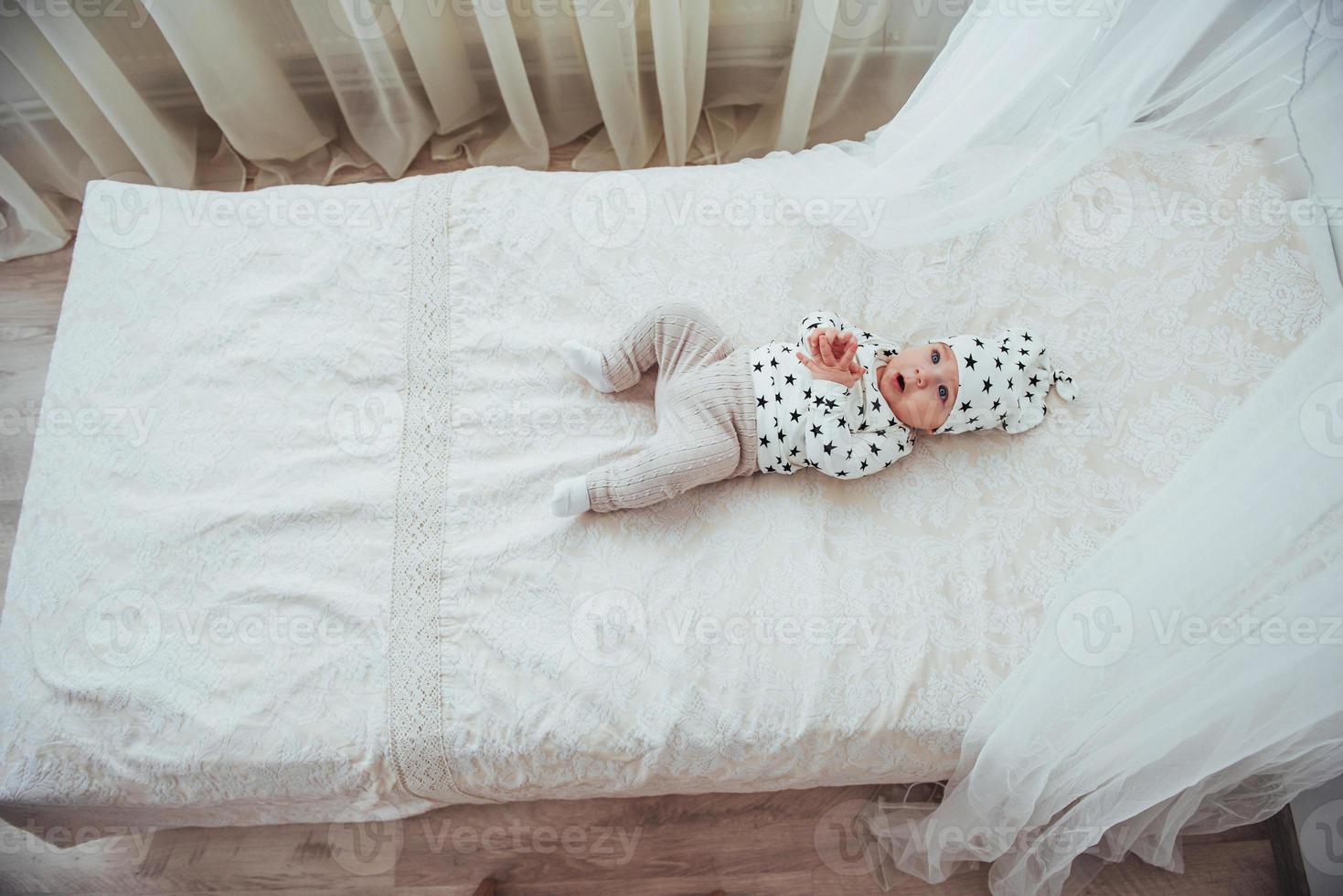 neugeborenes baby in einem weißen anzug und schwarzen sternen ist ein weißes weiches bett im studio foto