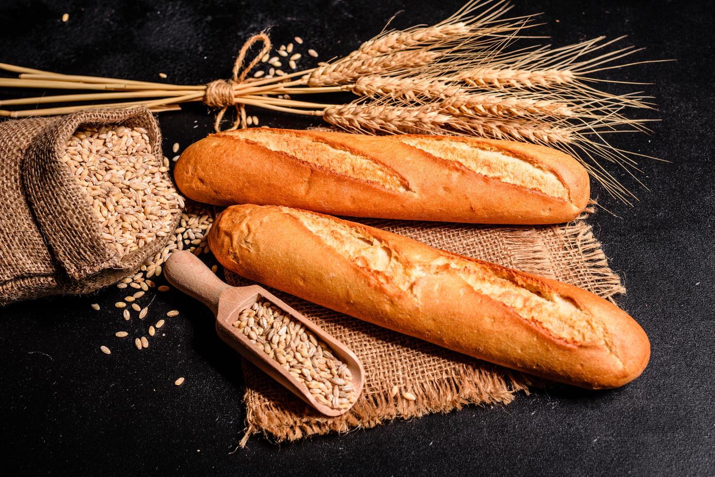 Schönes frisch gebackenes Brot mit Weizenkörnern auf dunklem Betonhintergrund foto