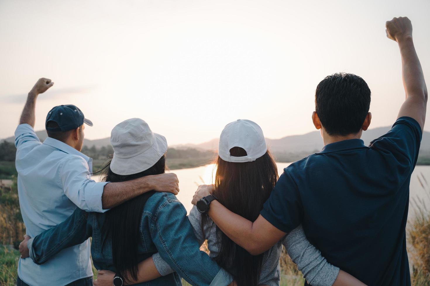 Gruppe von Menschen mit erhobenen Armen, die den Sonnenaufgang auf dem Berghintergrund betrachten. Glück, Erfolg, Freundschaft und Gemeinschaftskonzepte. foto