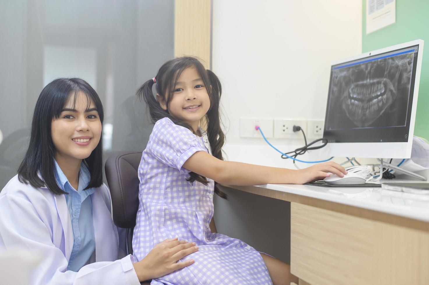 Zahnärztin erklärt einem kleinen Mädchen in der Zahnklinik die Röntgenaufnahme der Zähne, die Zahnuntersuchung und das Konzept der gesunden Zähne foto
