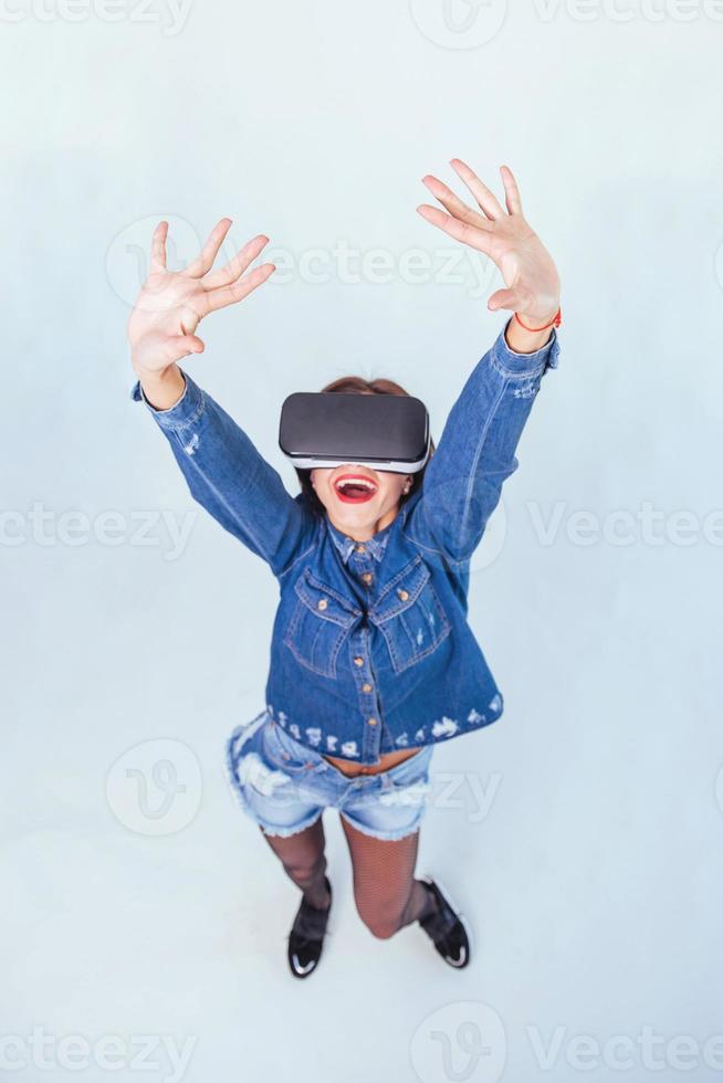 brünette schöne frau posiert im studio, trägt jeans und verwendet vr-brillen virtual-reality-headsets foto