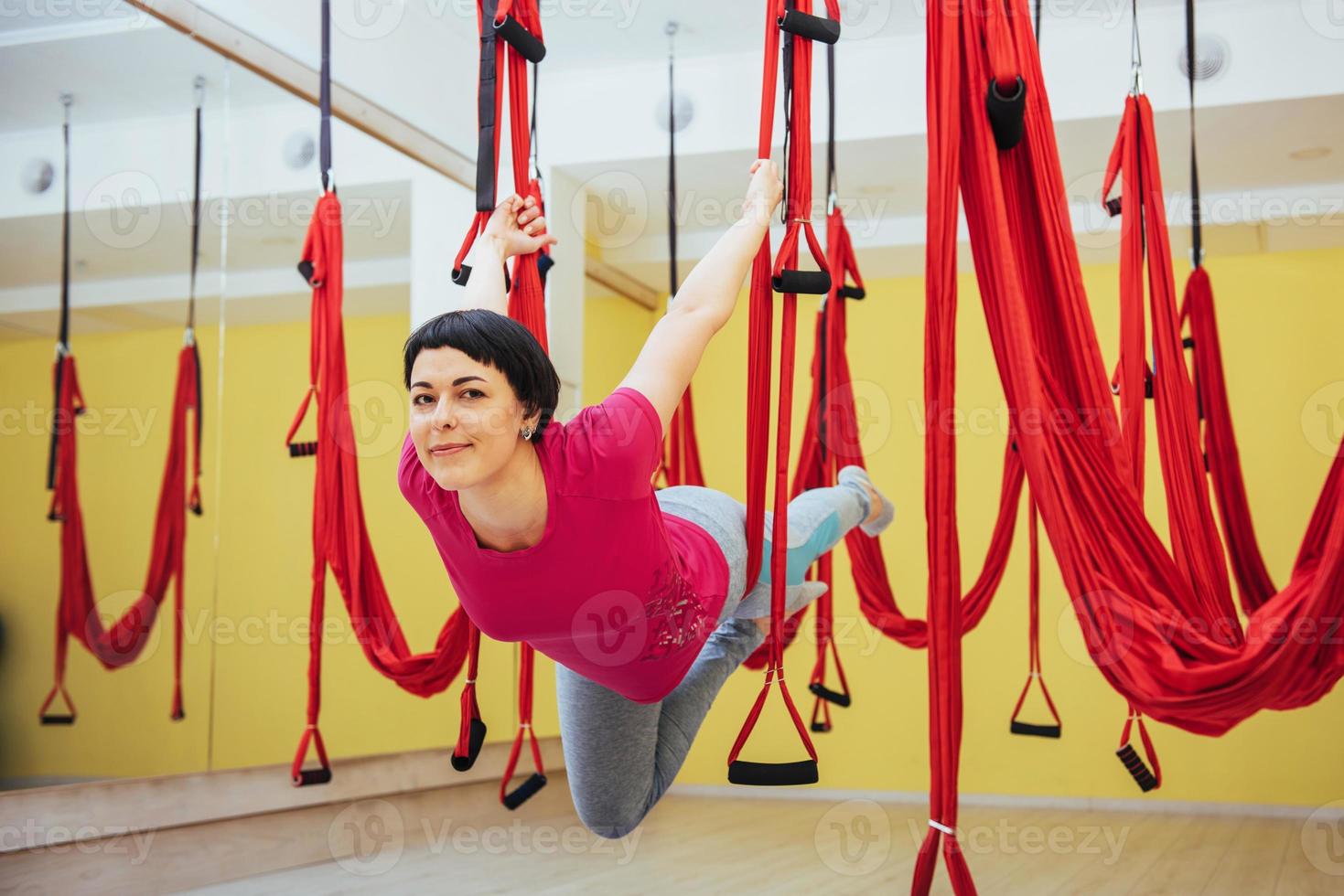 junge schöne frau, die yoga-fliege mit einer hängematte im studio praktiziert. foto