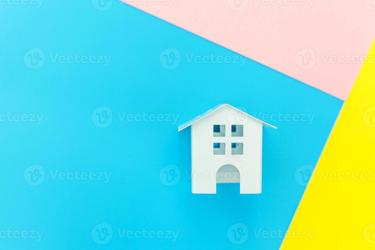 einfach design mit miniatur-weißem spielzeughaus isoliert auf blau gelb rosa pastell bunt trendy geometrischen hintergrund hypotheken-sachversicherung traumhaus konzept. flach liegend draufsicht kopierraum. foto