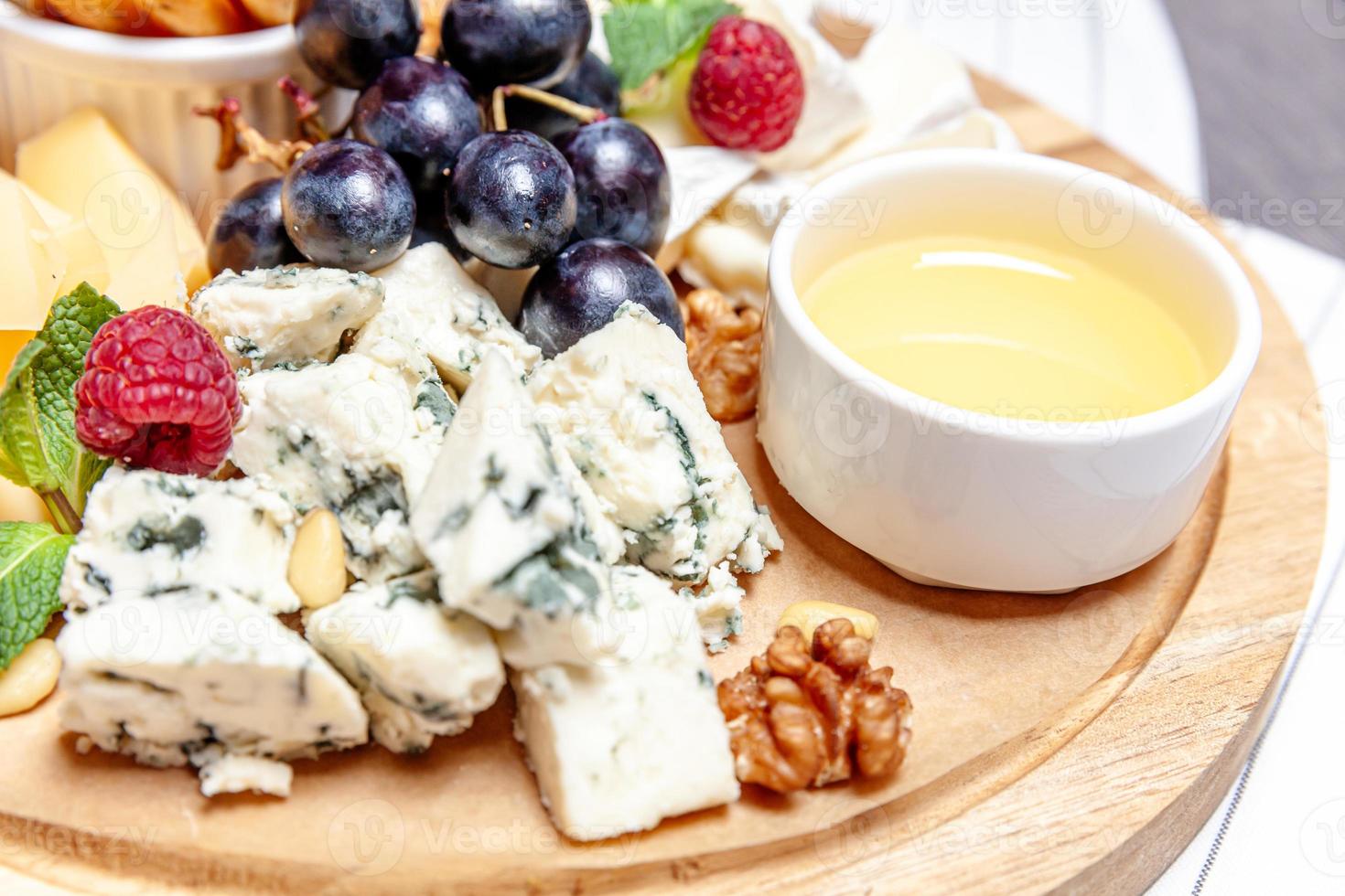 Brett mit verschiedenen Käsesorten. Käsemischungsset dor blu chedar parmesan brie honigsoße fingerbrot und traube auf wooren palte. Restaurantmenü Frühstücksteller. Gesundes Snack-Sortiment. foto