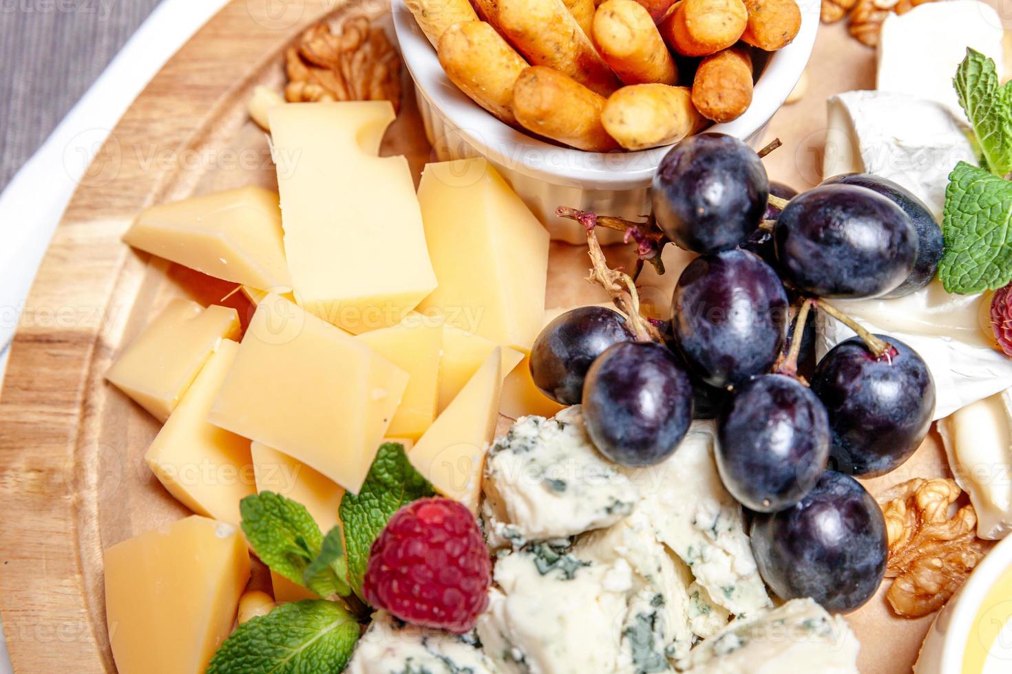 Brett mit verschiedenen Käsesorten. Käsemischungsset dor blu chedar parmesan brie honigsoße fingerbrot und traube auf wooren palte. Restaurantmenü Frühstücksteller. Gesundes Snack-Sortiment. foto