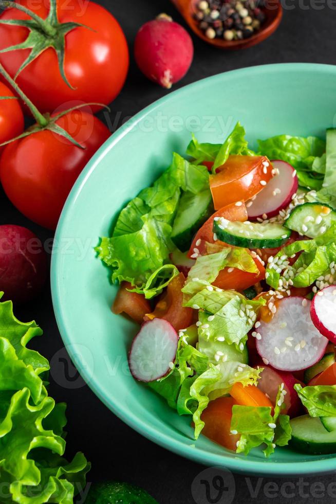 Salat aus frischem Gemüse in einer Keramikschale auf grauem Hintergrund. Saisonales Sommergericht aus Tomaten, Gurken und Radieschen. foto