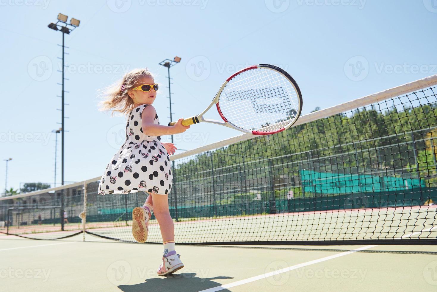 süßes kleines Mädchen, das draußen auf dem Tennisplatz Tennis spielt foto