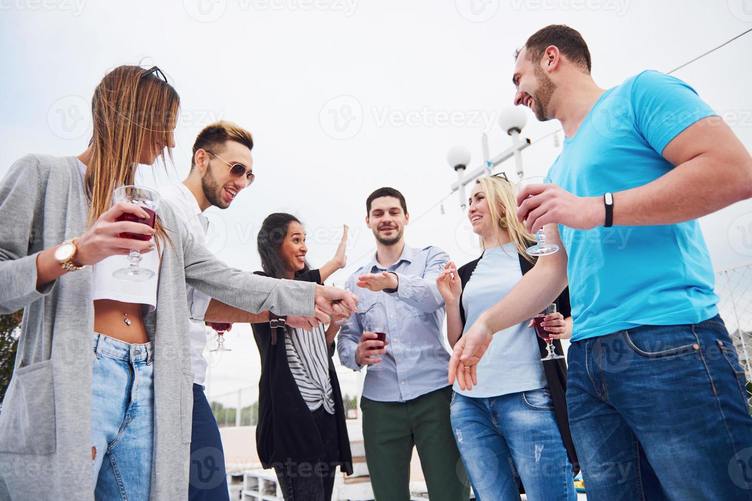 Porträt einer Gruppe junger Menschen, die am Rand der Seebrücke sitzen, draußen in der Natur. Freunde, die ein Spiel auf dem See genießen. foto