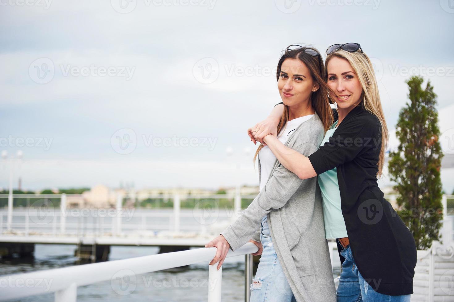 Fröhliches junges Mädchen in stilvollen Bekleidungsmarken auf dem Pier in der Nähe des Wassers foto