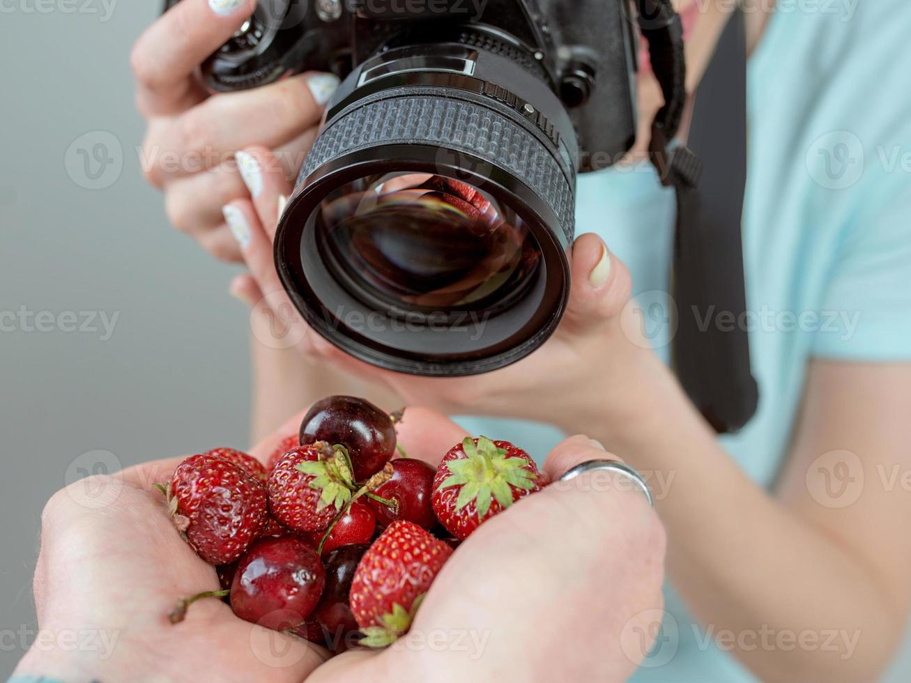 Fotografin der jungen Frau, die mit Digitalkamera Erdbeeren und Kirsche in den Händen schießt. nahaufnahme, schießen, hobby, essen, berufskonzept foto