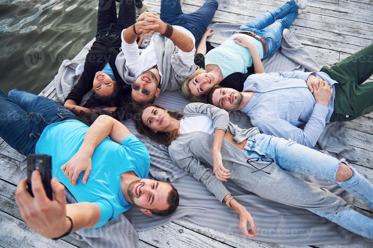Gruppe schöner junger Leute, die Selfies machen, die auf dem Pier liegen, die besten Freunde von Mädchen und Jungen mit Vergnügen Konzept schafft emotionales Leben der Menschen. foto
