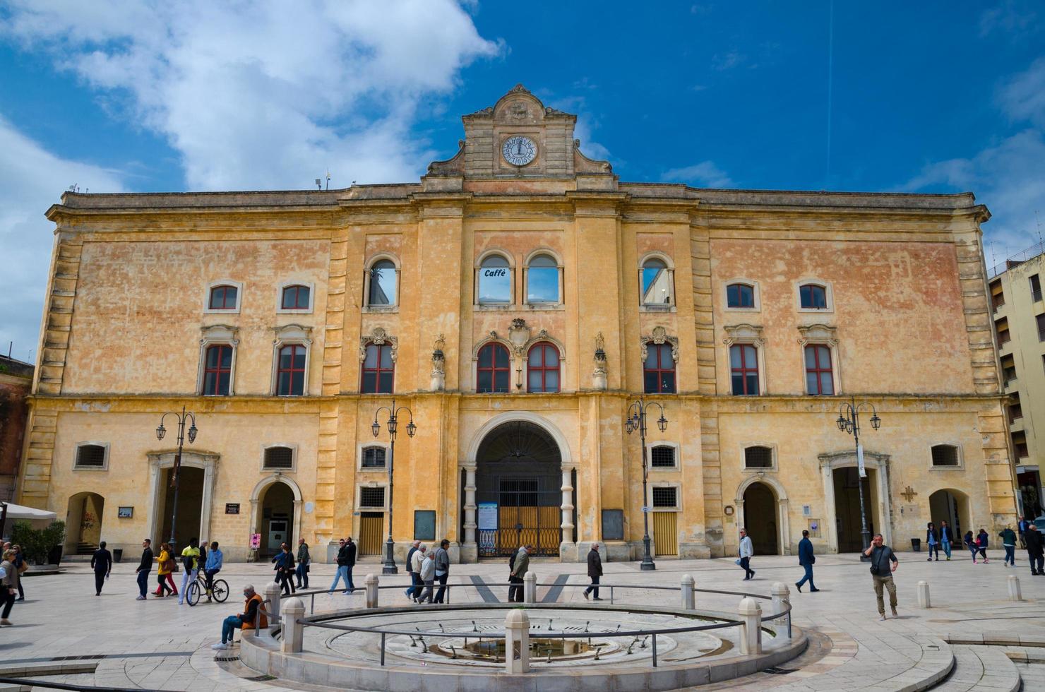 Matera, Italien - 6. Mai 2018 Menschen zu Fuß in der Nähe von Cinema Comunale Palazzo dell'annunziata Palast mit Uhr an der Fassade und Brunnen auf der Piazza Vittorio Veneto Platz blauer Himmelshintergrund foto