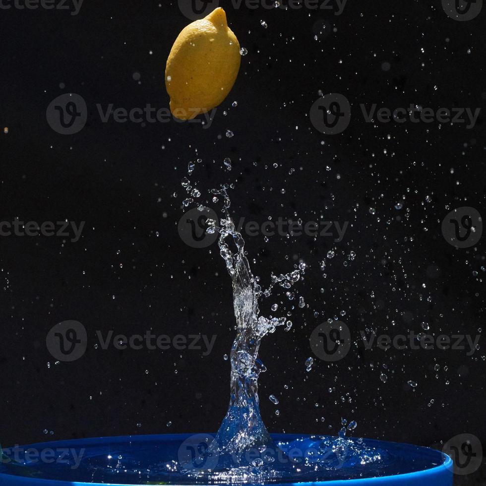 saftige gelbe zitrone fällt in wasser auf schwarzem hintergrund foto