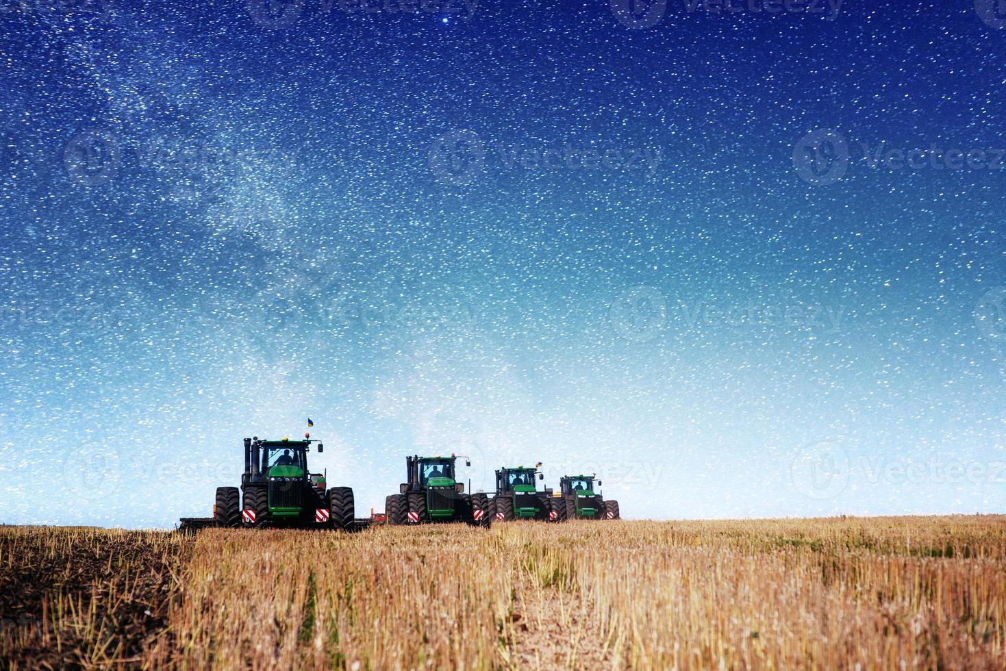 traktor, der bauernhoffeld in vorbereitung für das frühlingspflanzen pflügt. fantastischer Sternenhimmel und die Milchstraße foto