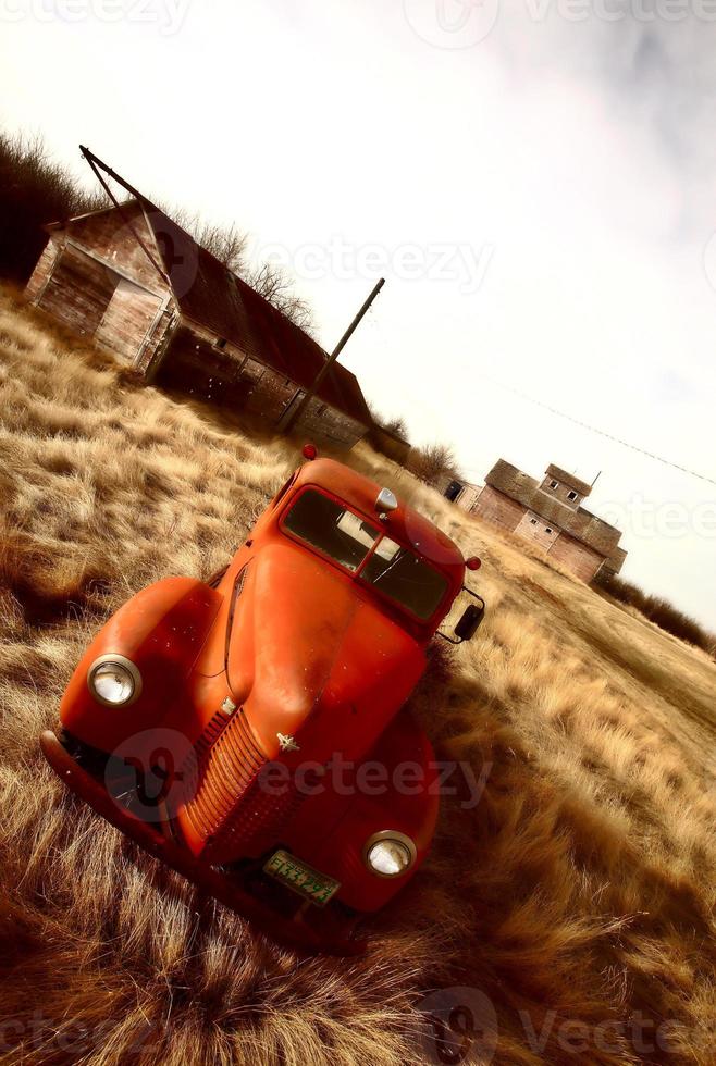 Alter landwirtschaftlicher Lastwagen, der in der Nähe von ungenutzten Holzgebäuden aufgegeben wurde foto