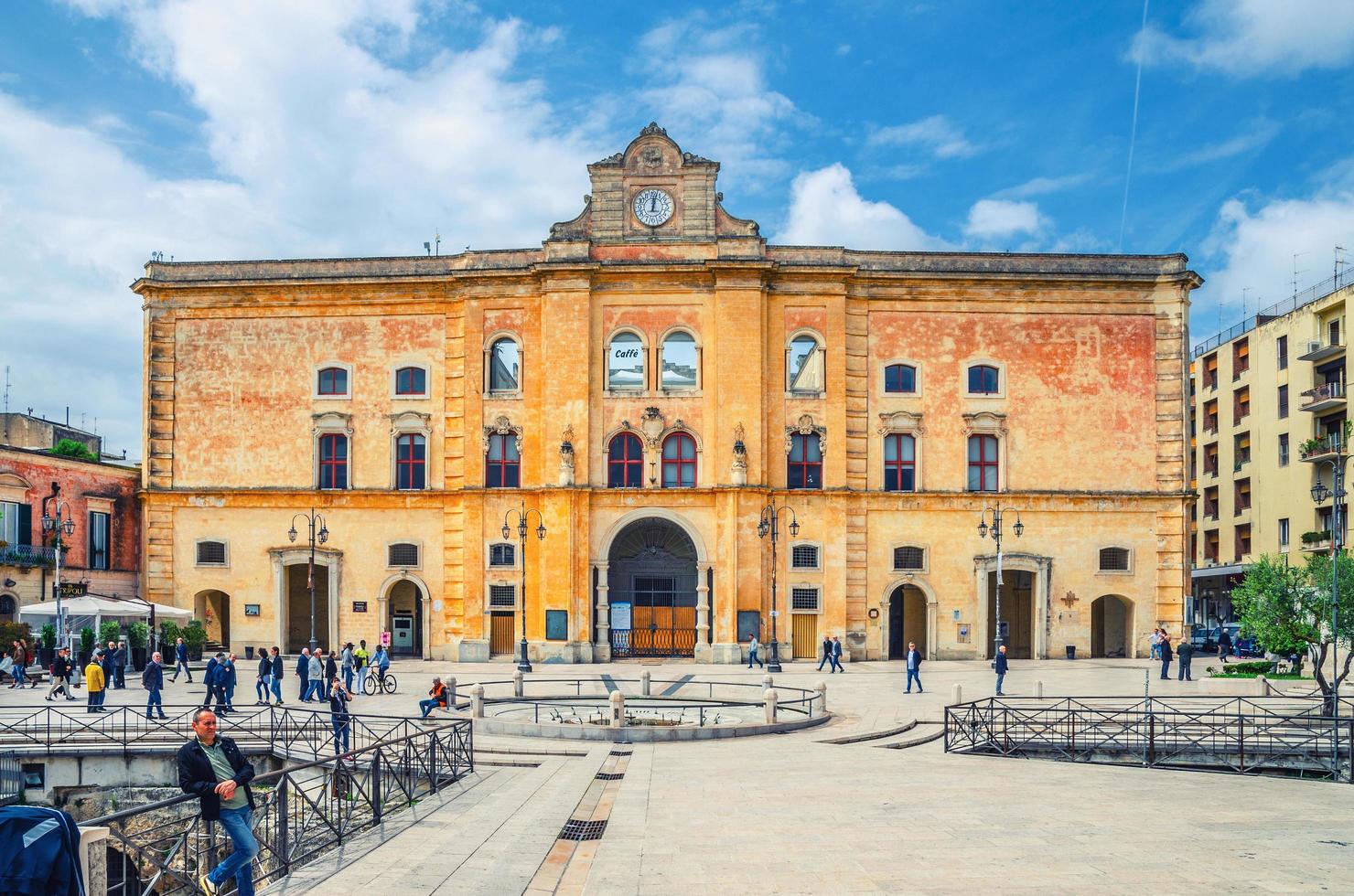 leute, die in der nähe des kinos comunale palazzo dell'annunziata palast mit uhr an der fassade und brunnen auf der piazza vittorio veneto hinuntergehen foto