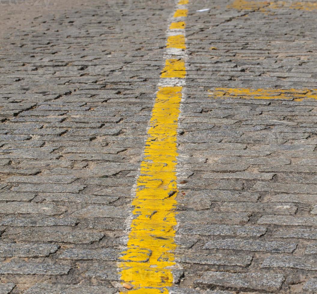 Textur von dunkelgrauen Kopfsteinpflaster mit gelben Streifen als Straßenmarkierung foto