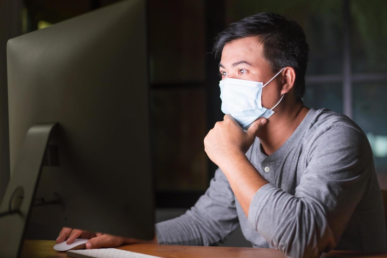 mann, der eine vorbeugende maske trägt und nachts von zu hause aus arbeitet, wenn eine corona-viruserkrankung vorliegt. arbeit von zu hause und gesundes konzept foto