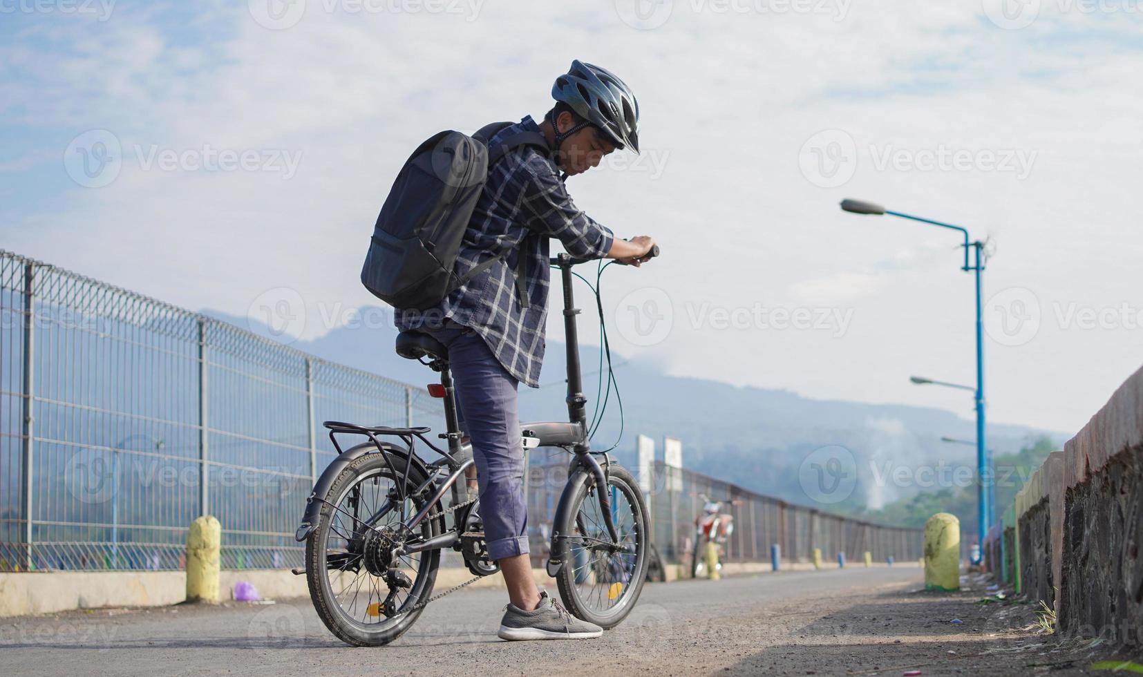 asiatischer junger mann mit rucksack, der sich nach der fahrradfahrt ausruht foto