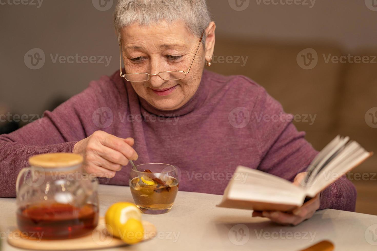 Frau sitzt am Tisch, trinkt Tee mit Zitrone und liest ein Buch foto