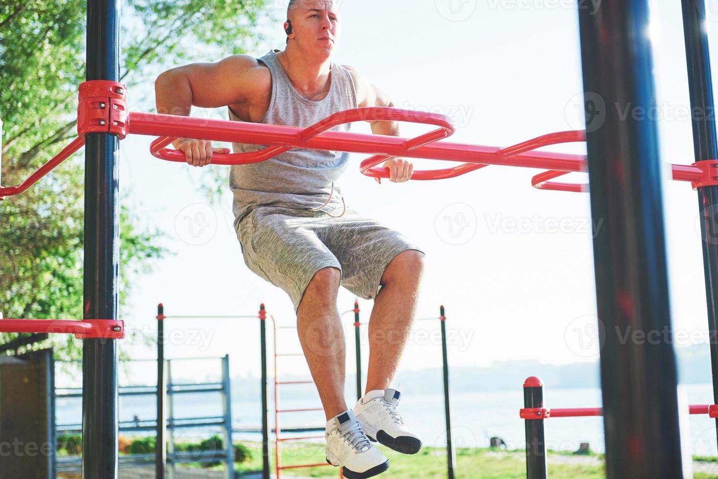 muskulöser Mann mit schönem Oberkörper, der auf horizontalen Balken auf einem verschwommenen Parkhintergrund trainiert. junger Mann, der im Freien Klimmzüge macht foto