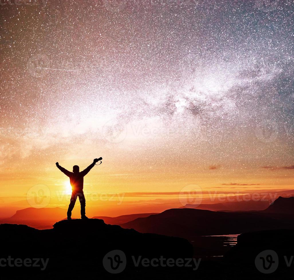 Die Silhouette einer Frau steht auf einem Berg und zeigt vor Sonnenaufgang auf die Milchstraße und genießt den farbenfrohen Nachthimmel foto